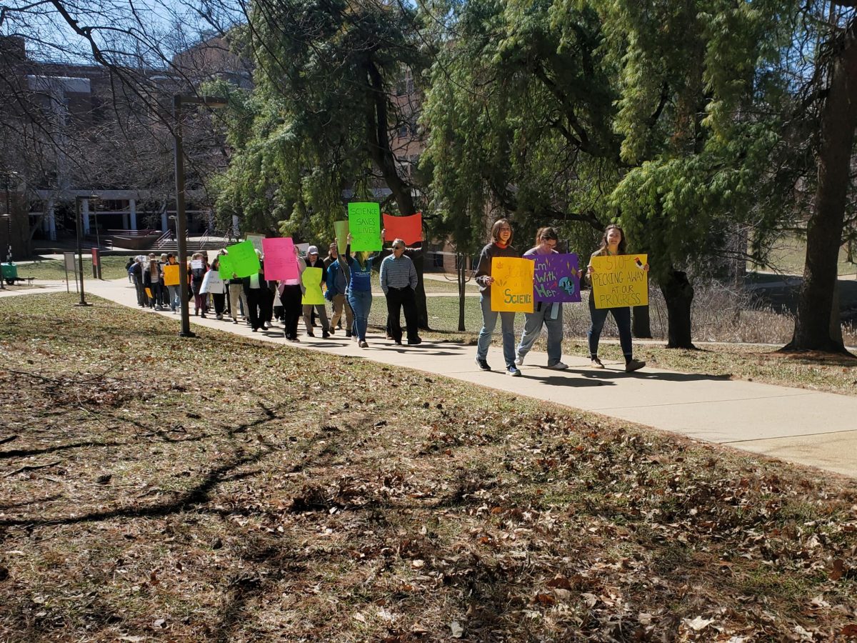 students walking, holding signs during a Stand Up for Science demonstration on the UMSL campus.