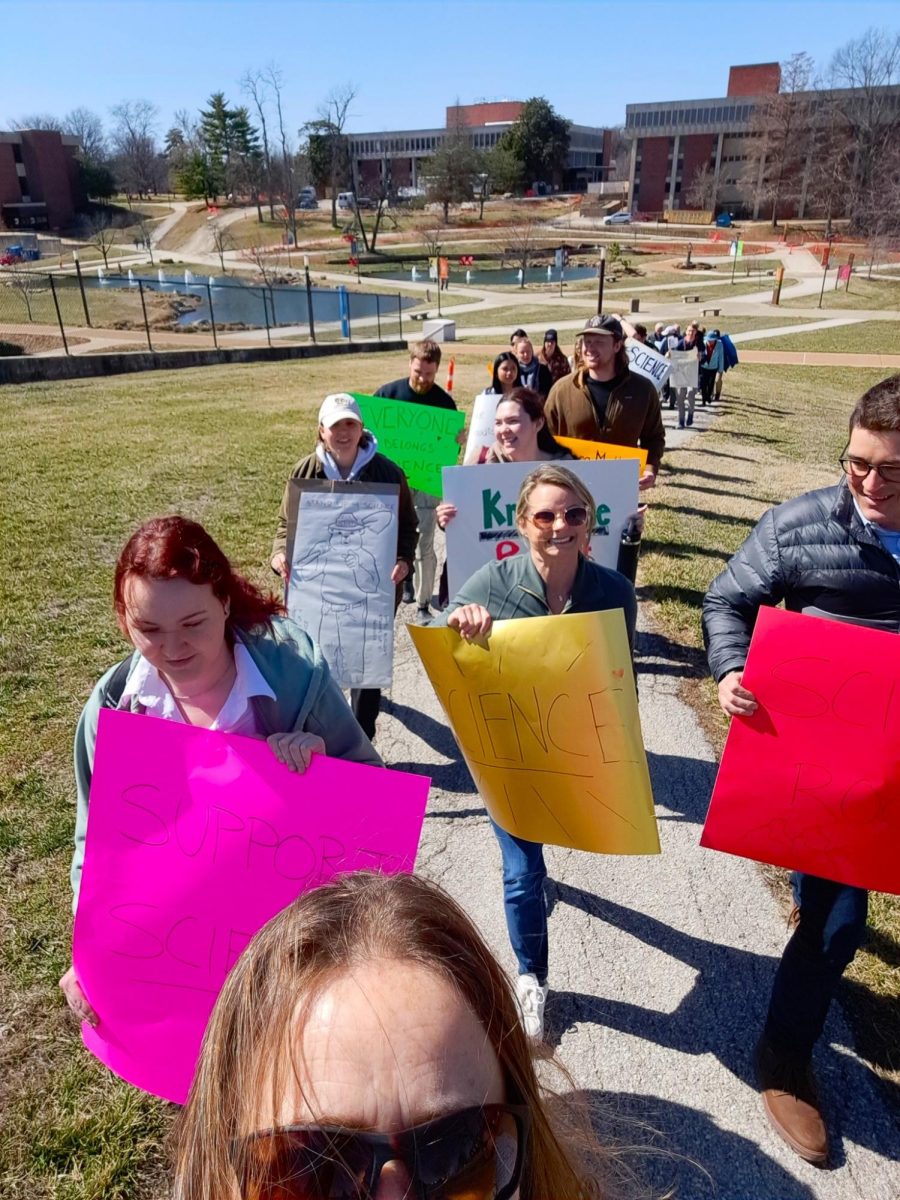 group of students and faculty walking on UMSL campus, holding signs supporting science