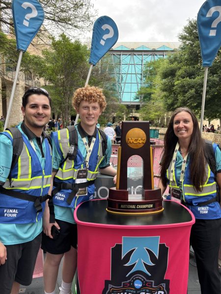 Andrew Price, Charlie Farris, and Karen Boleska standing next to the NCAA March Madness National Champion Trophy